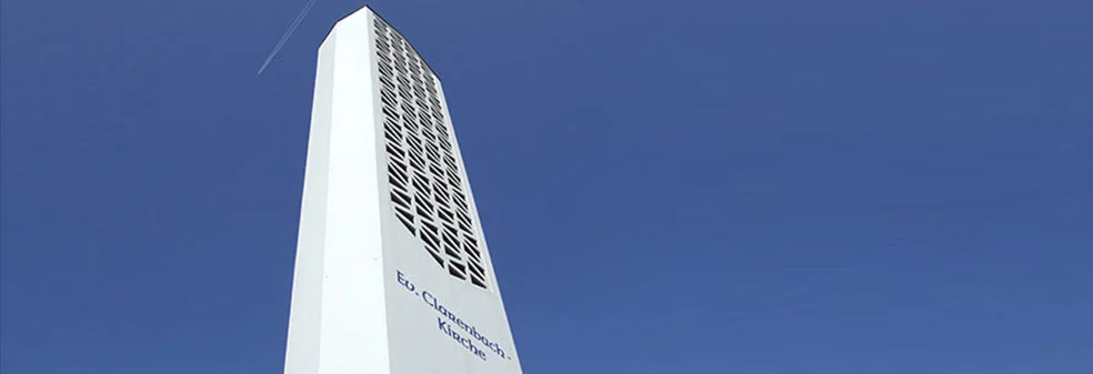 Weißer Turm der Clarenbachkirche vor blauem Himmel.