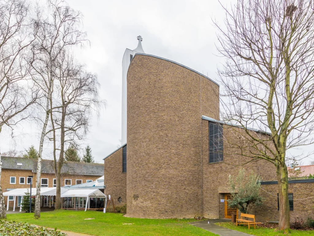 Außenansicht der Dietrich-Bonhoeffer-Kirche in Junkersdorf mit gerundeter Backsteinwand und Kreuz.