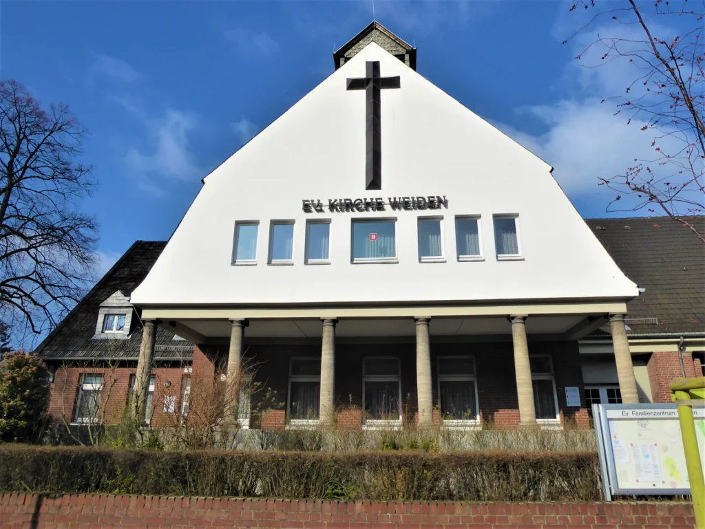Giebelfassade der Evangelischen Kirche Weiden mit großem Kreuz und überdachtem Eingang.